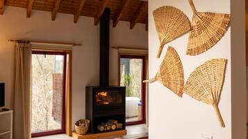 A cozy living room with a fireplace, large windows, and a wall-mounted fan.