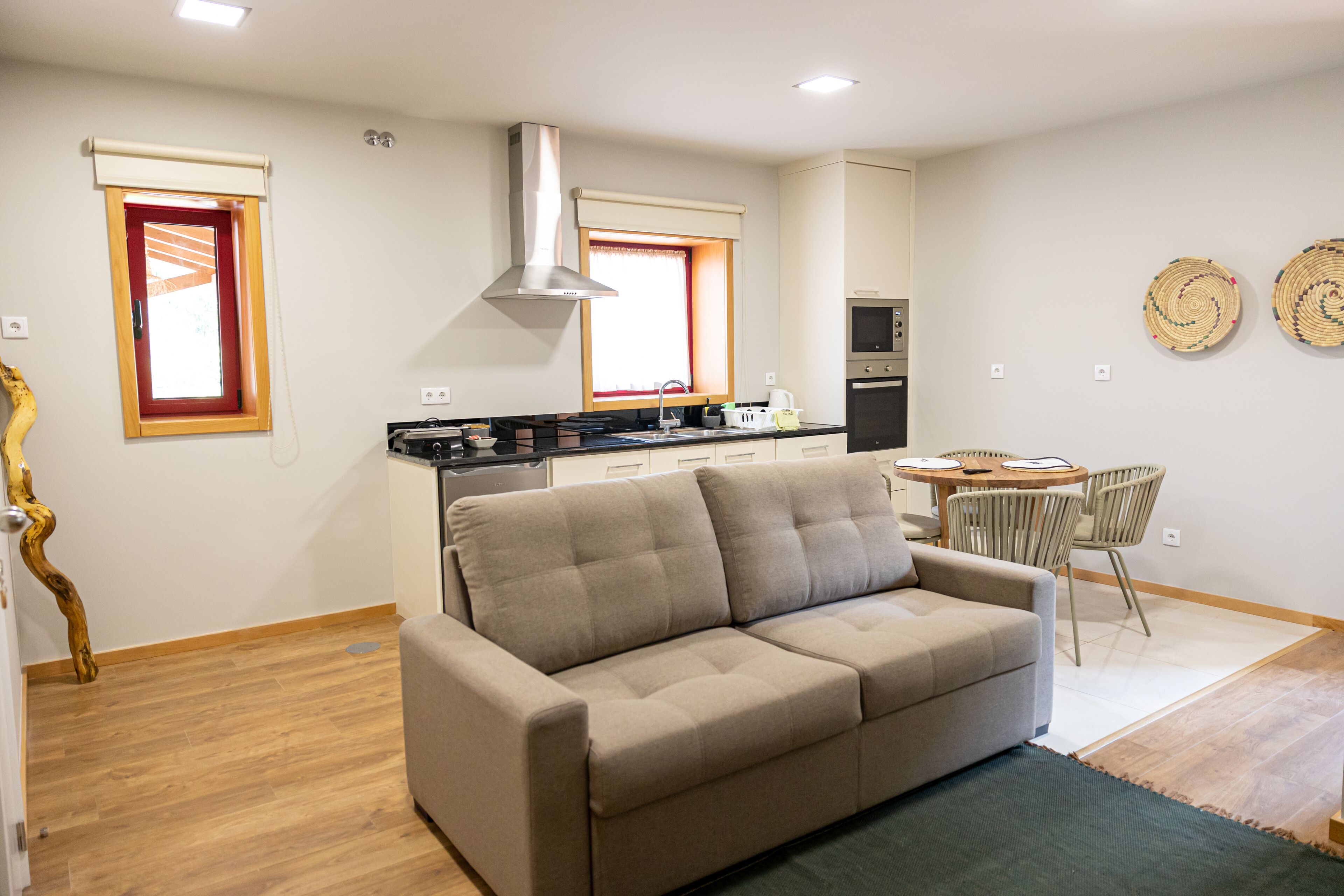 A modern kitchen with a built-in oven, a dining area with a round table and chairs, and a sofa in the living area.