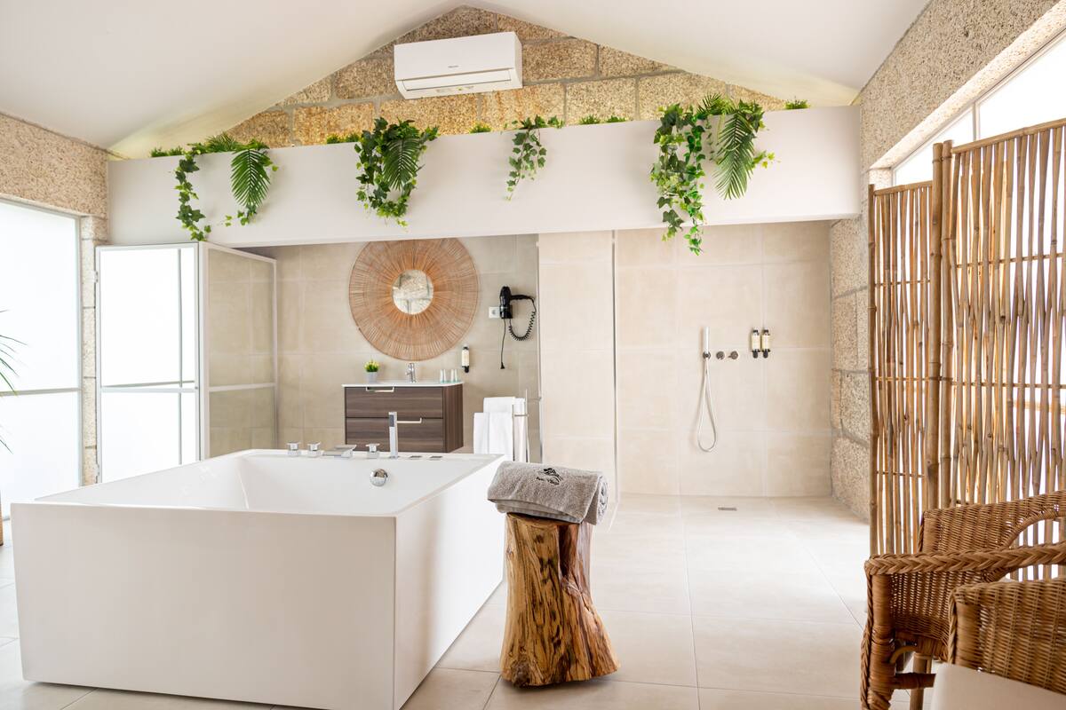 A modern bathroom with a large bathtub, a wooden stool with a towel, a mirror, and a shower area.