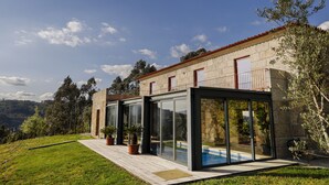 A modern house with a stone facade, large glass windows, and a wooden deck. - Peso Village (Amarante)
