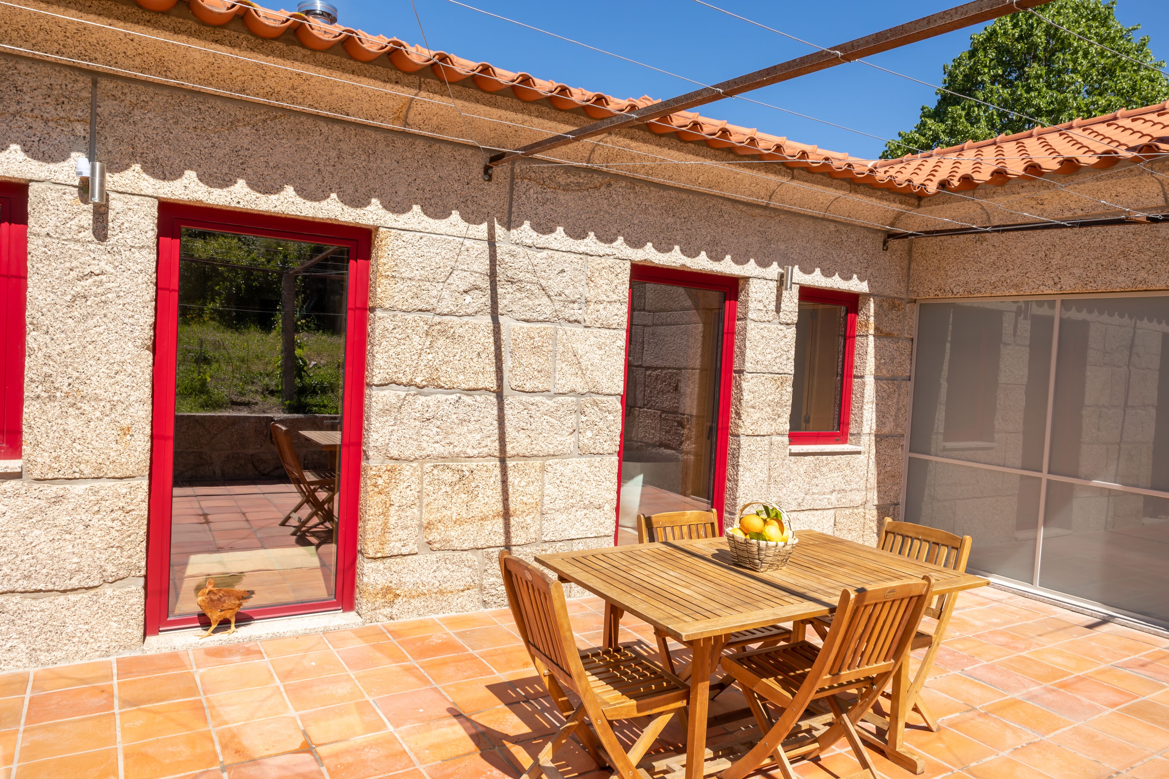 A patio with a wooden table and chairs, a red-framed door, and a tiled floor.