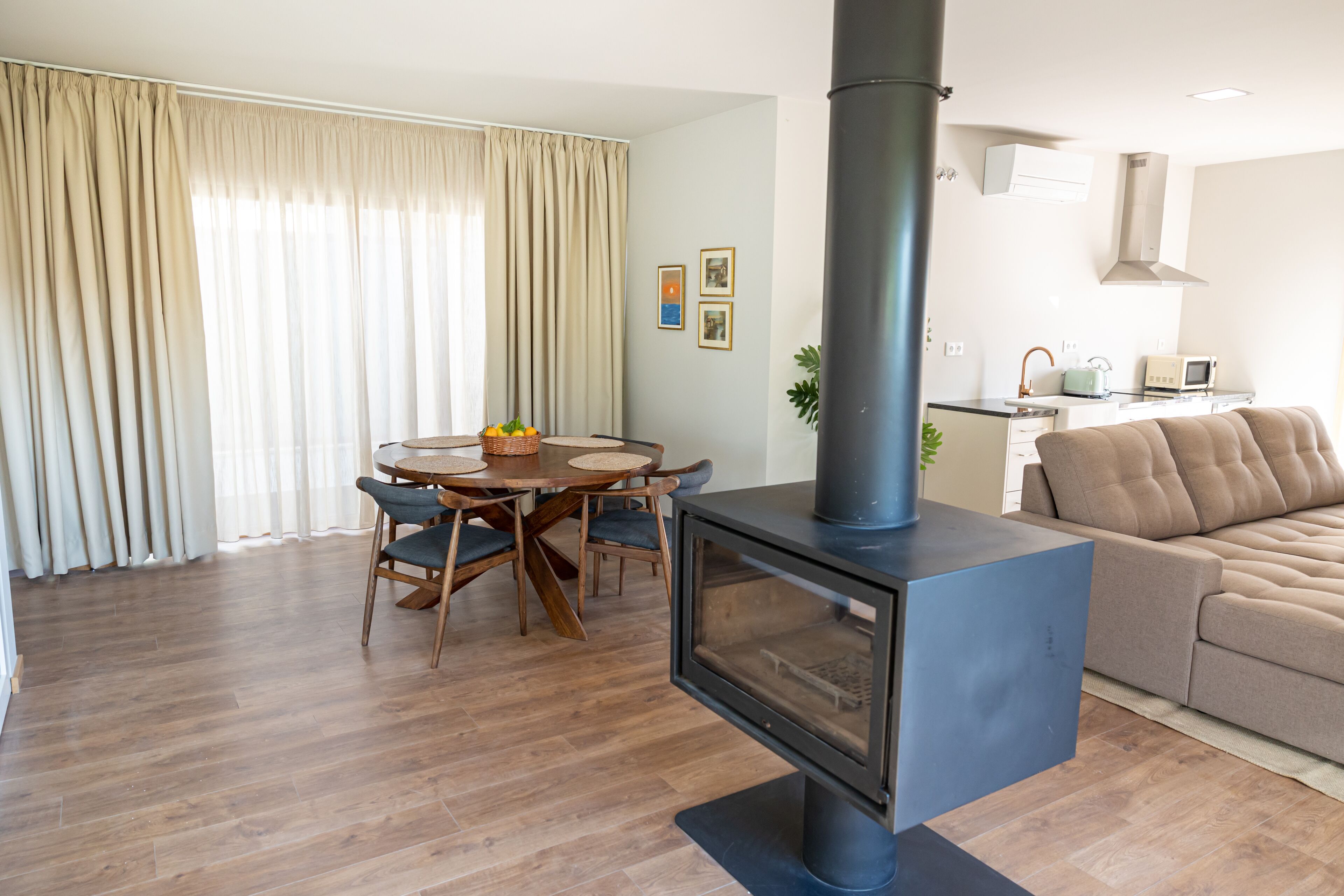 A modern living room with a wood-burning stove, a dining area with a round table and chairs, and a kitchen area with a microwave and toaster.