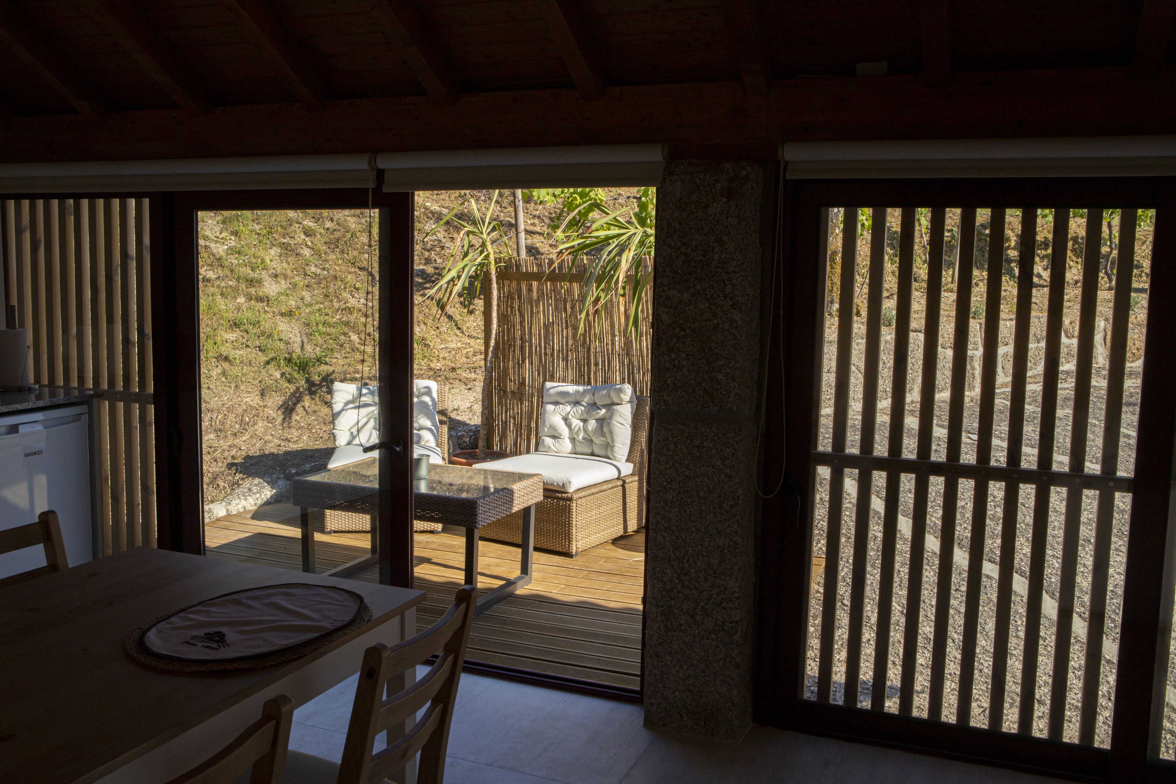 Un comedor con mesa y sillas, un sofá de mimbre y vistas del patio exterior a través de una puerta corredera.
