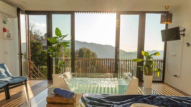 A spa room with a hot tub, a wooden bench, a massage table, and a view of the outdoors. - Peso Village (Amarante)