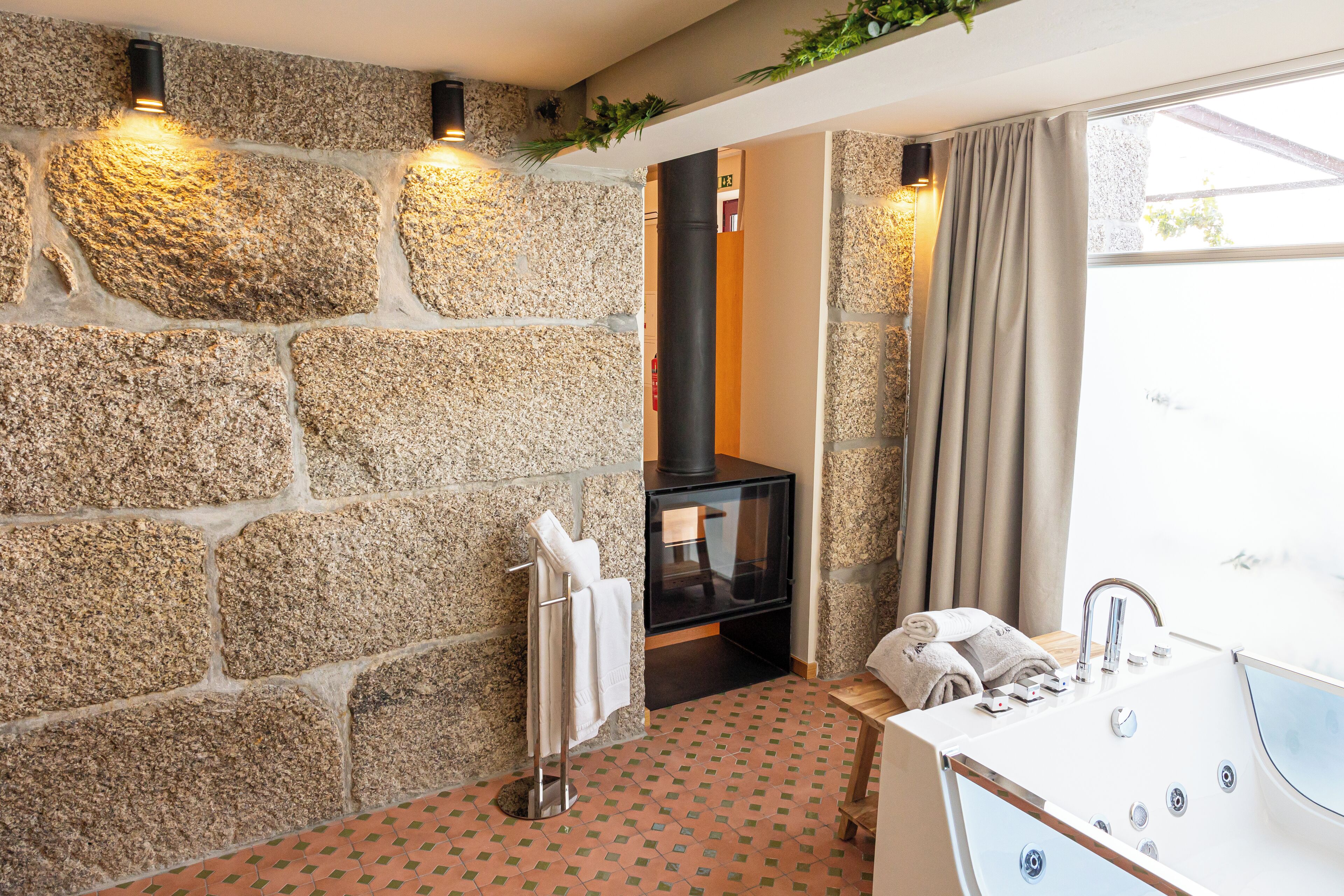 Un baño con pared de piedra, chimenea empotrada, bañera y ventana con cortinas.