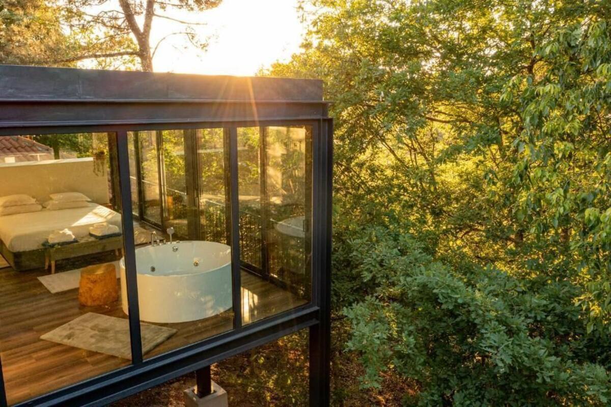 A glass-enclosed outdoor bedroom with a bathtub, a bed, and a seating area.