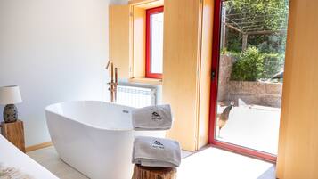 Une salle de bain moderne avec une baignoire sur pieds, un tabouret en bois avec des serviettes, et une vue sur un paon à l’extérieur.