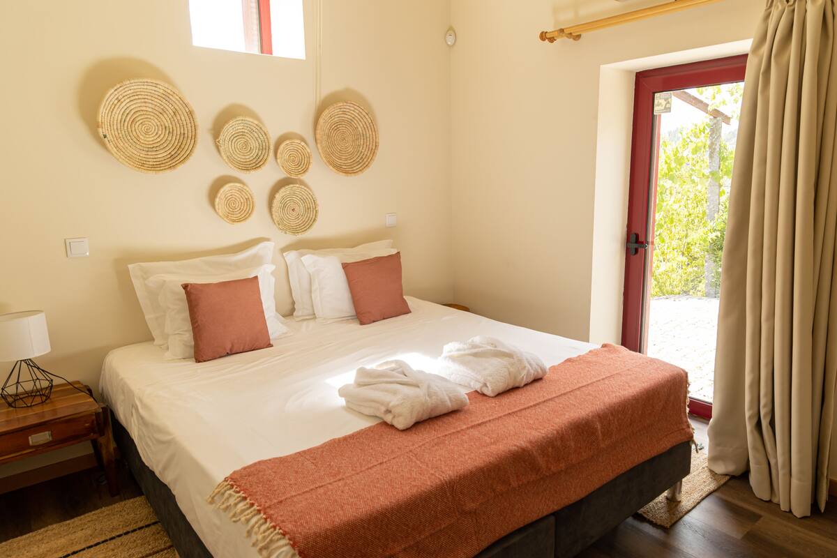 A neatly made bed with white and pink pillows, a brown throw blanket, and a wooden nightstand with a lamp.