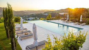 A swimming pool with lounge chairs and umbrellas, surrounded by greenery and hills in the background. - Peso Village (Amarante)