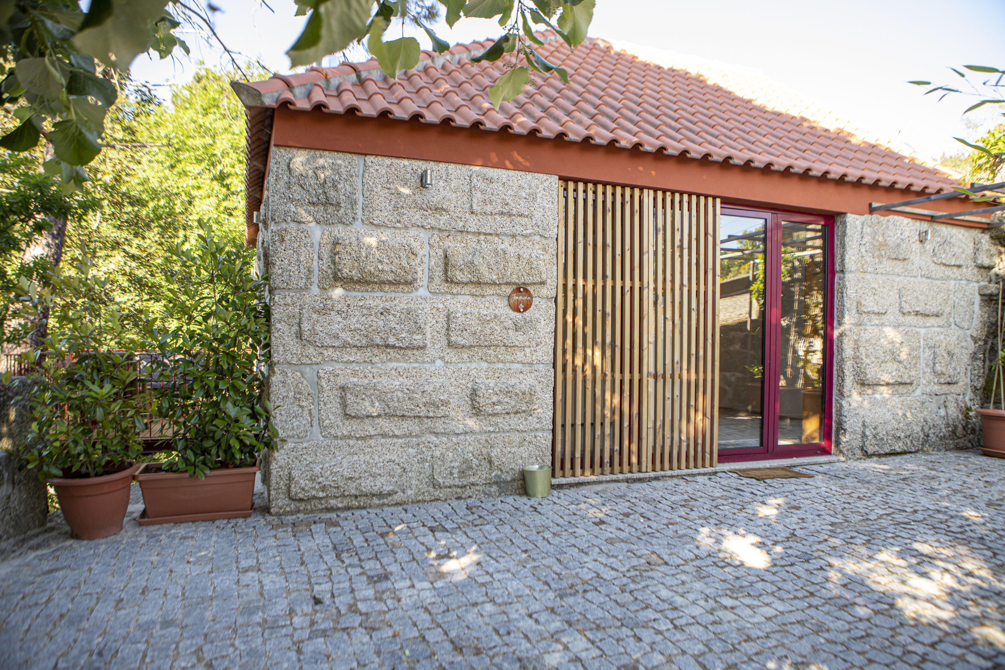 A stone building with a tiled roof, a wooden door, and potted plants.