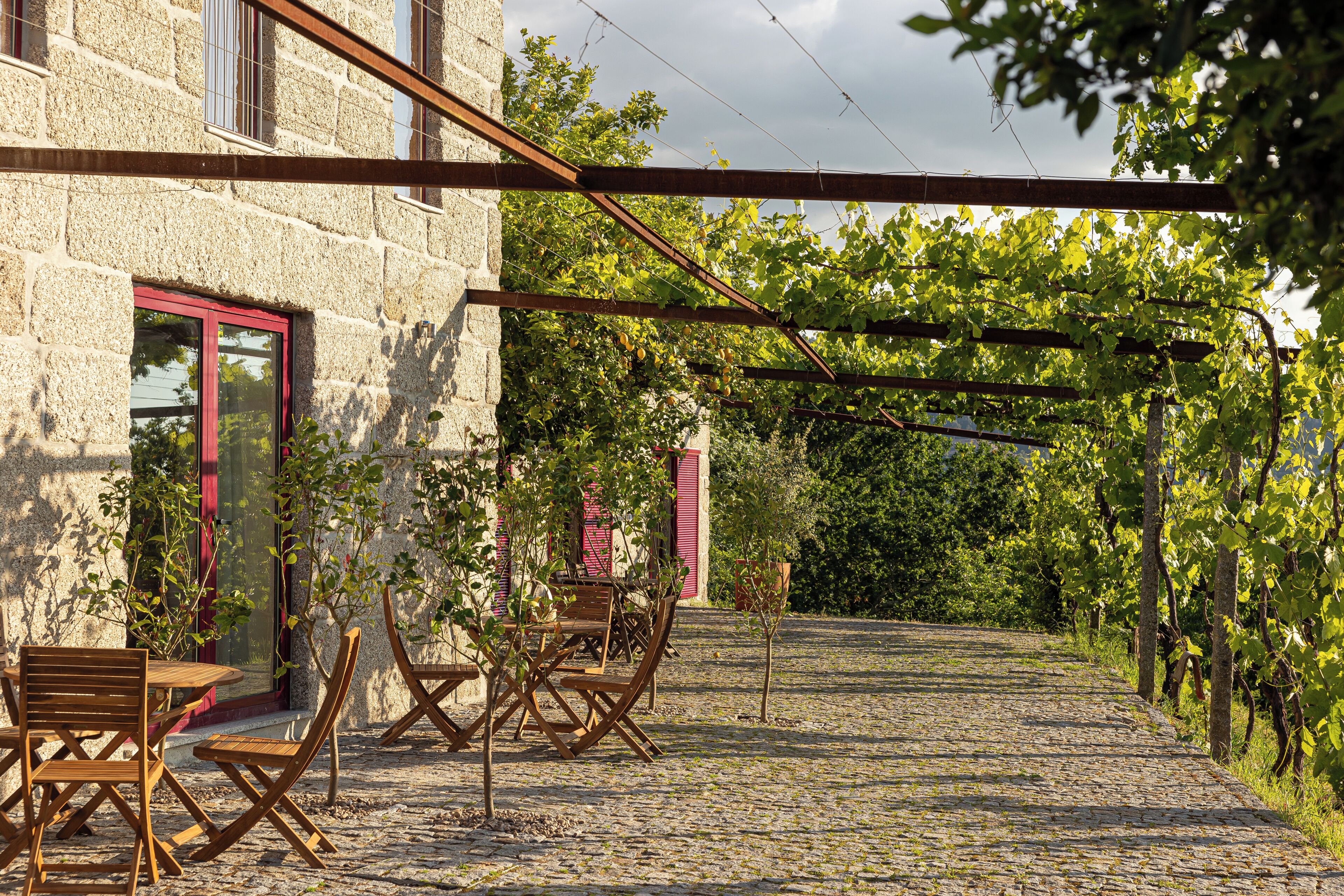 A stone building with a red door, outdoor seating, and a vineyard in the background.
