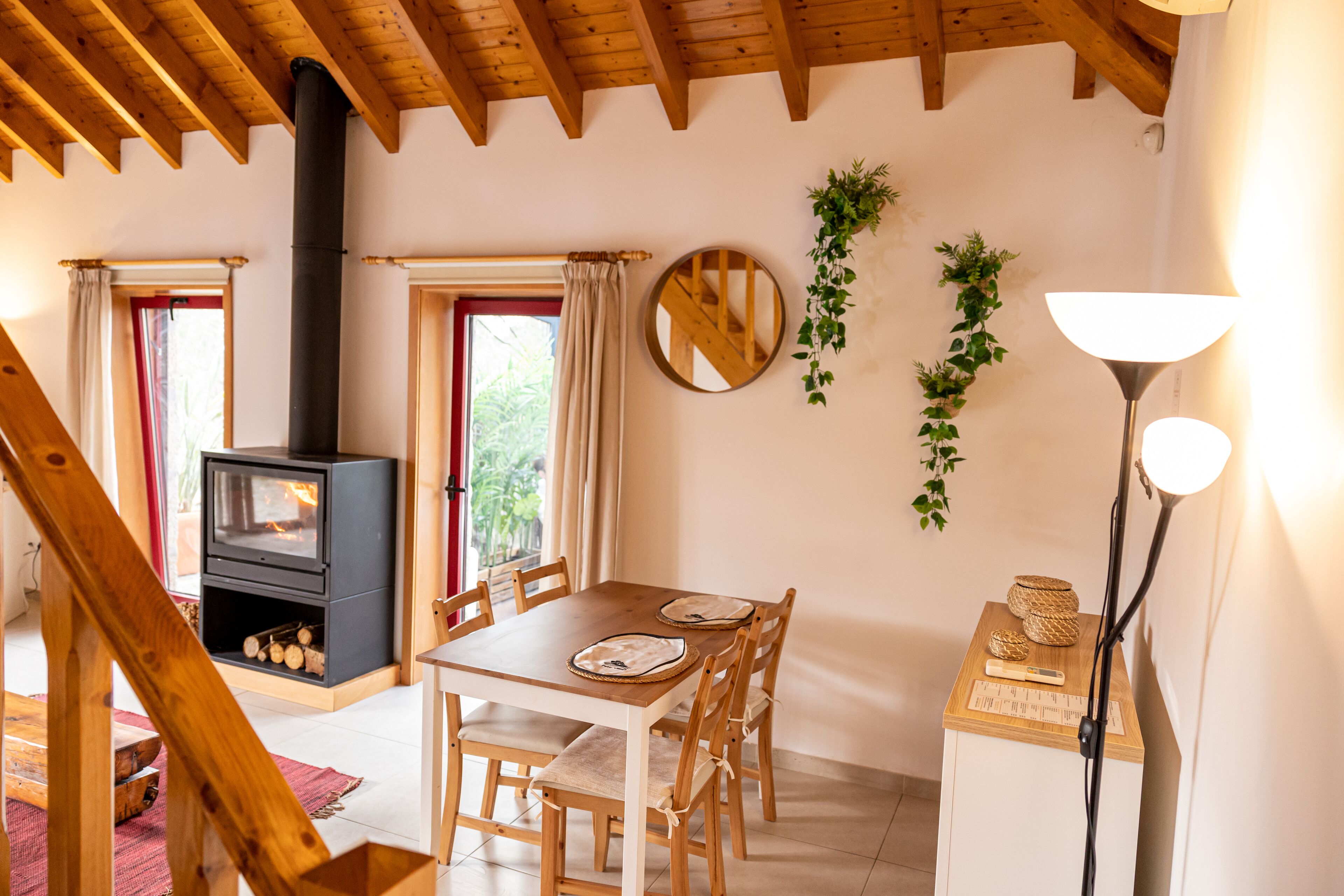 Una habitación acogedora con techo de madera, chimenea, una mesa de comedor con sillas y una lámpara.