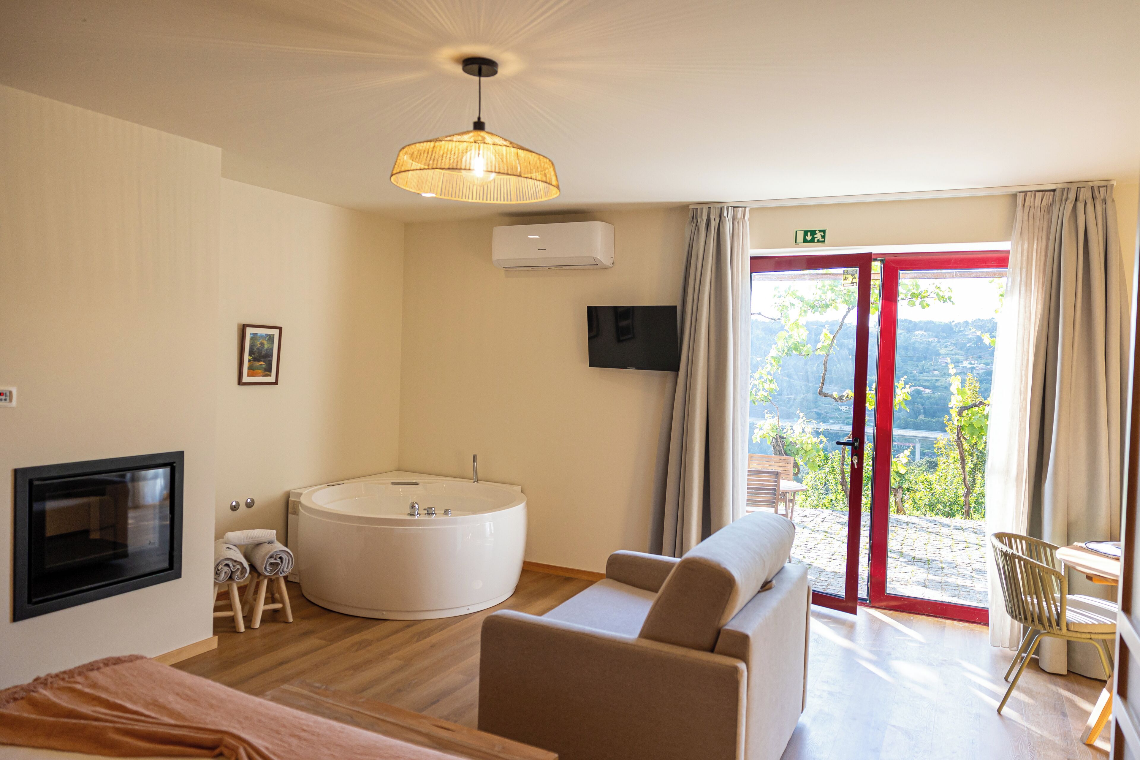 Ein modernes Hotelzimmer mit einer runden Badewanne, einem Sofa, einem Fernseher und Blick auf eine gebirgige Landschaft durch eine Glastür.