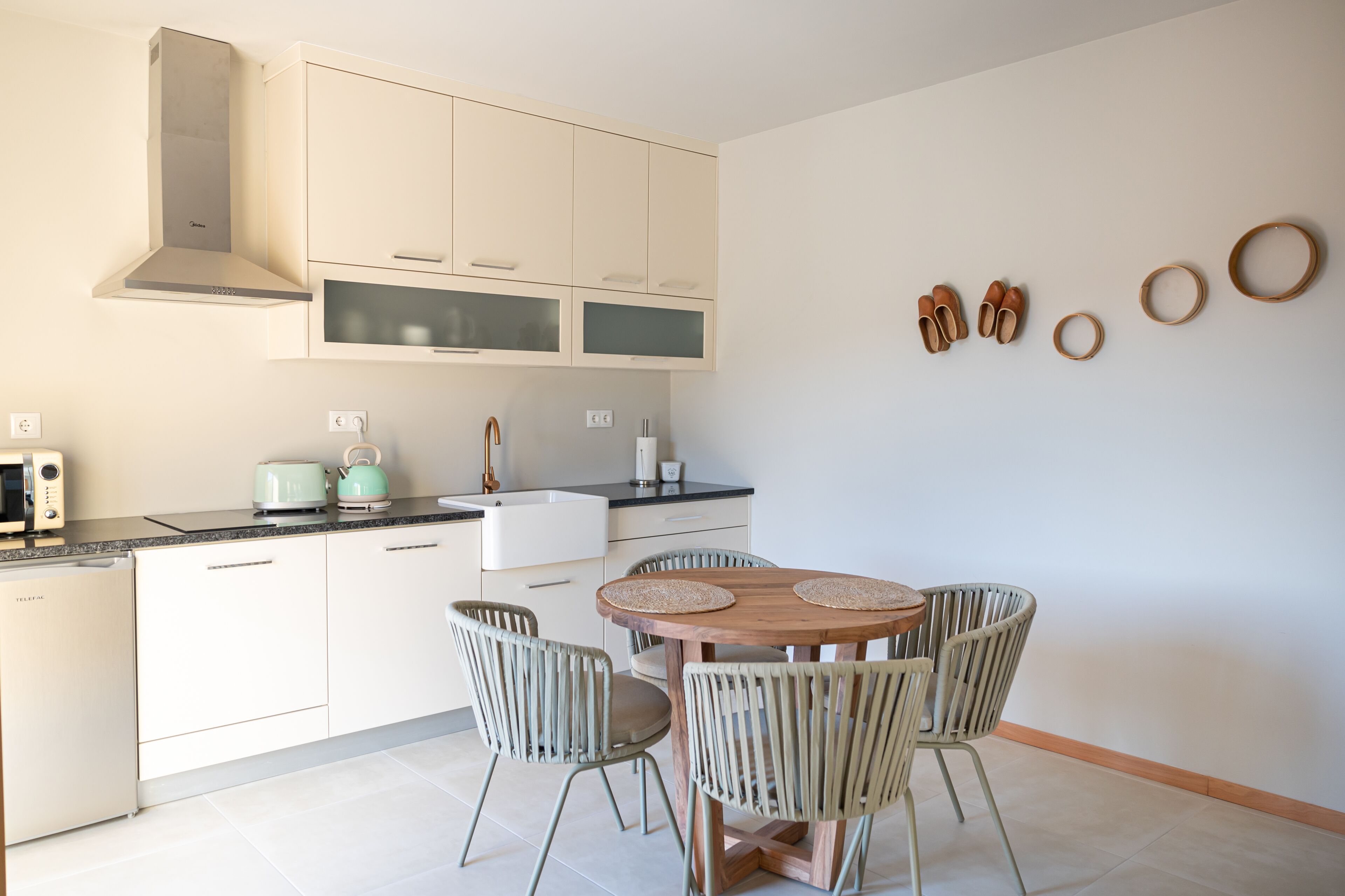 Une cuisine moderne avec des armoires blanches, un four encastré et un coin repas comprenant une table en bois et des chaises en osier.