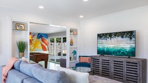A living room with a gray sofa, a coffee table, a TV, and a large painting of a beach scene.