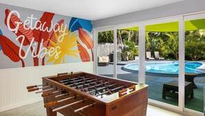 A room with a foosball table, a pool, and a mural with tropical leaves and the words "Getaway Vibes".