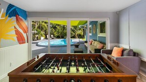 A room with a foosball table, a pool, and a view of the outdoors.