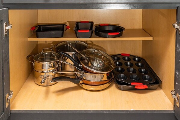 Un meuble de cuisine contenant des casseroles et des poêles en acier inoxydable, ainsi qu’un moule à muffins.