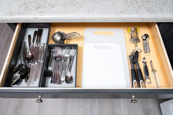 A drawer with neatly organized kitchen utensils including knives, forks, spoons, and a cutting board.