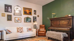 A living room with a white sofa, a brown leather chair, a grand piano, and a patterned rug.