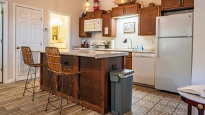A kitchen with wooden cabinets, a microwave, a refrigerator, and a bar stool.