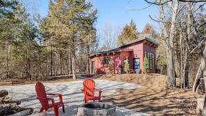 A cabin with a gravel patio, two red Adirondack chairs, and a stone fire pit. - Romantic Cabin - Lakeside (Jonesburg)