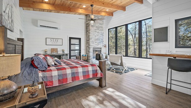 A bedroom with a large bed, a fireplace, and a view of trees through large windows. - Romantic Cabin - Lakeside (Jonesburg)