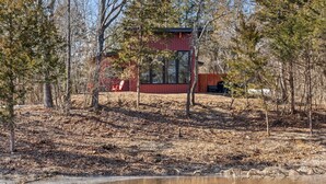 A cabin with a red exterior, surrounded by trees and a pond. - Romantic Cabin - Lakeside (Jonesburg)