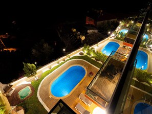 A rooftop pool area with multiple swimming pools and lounge chairs, surrounded by landscaped gardens and illuminated by night lighting. - Alanya Luxury Villas (Alanya)