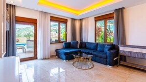 A modern living room with a sectional sofa, a glass coffee table, and large windows offering a view of the outdoors. - Alanya Luxury Villas (Alanya)