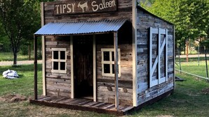 A wooden structure labeled "TIPSY Saloon" with a rustic exterior and a metal roof.