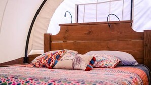 A bed with a wooden headboard, colorful bedding, and a tent-like structure in the background.