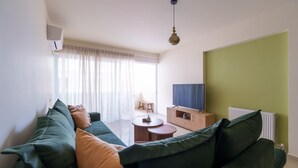 Ein Wohnzimmer mit einem grünen Sofa, einem kleinen Holztisch und einem Fernseher auf einer Holzkommode.