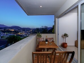 A balcony with a wooden table set for two, a bottle of champagne, and two glasses. - Oikies. Luxury Apartment with Lake View | private free parking area (Agios Nikolaos)