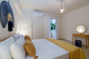 A bedroom with a bed, a bedside table with a mirror, and a view to the outside.