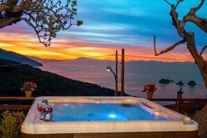 A hot tub with a scenic view of a sunset over a body of water and mountains.