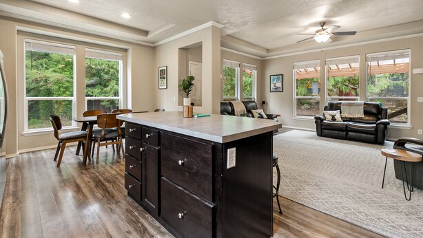 A spacious kitchen with a large island, dining area with chairs, a sofa, and a view of greenery through large windows. - Hart Haus at Stevens Pass- spacious w/ hot tub, EV charger, close to hikes! (Skykomish)