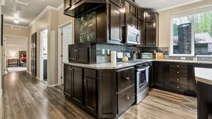 A kitchen with dark wood cabinets, a granite countertop, and a large island with a built-in oven. - Hart Haus at Stevens Pass- spacious w/ hot tub, EV charger, close to hikes! (Skykomish)