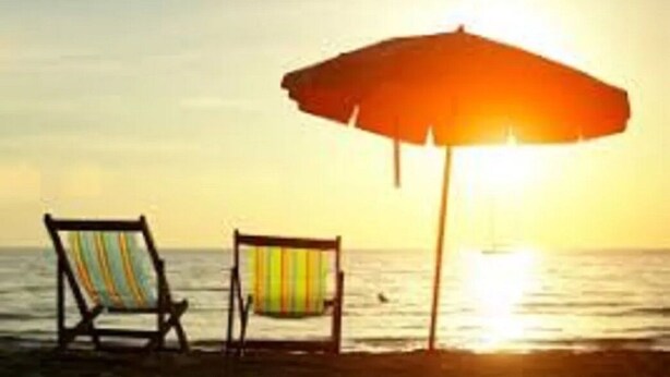Duas cadeiras de praia e um guarda-sol numa praia arenosa, com o oceano ao fundo.