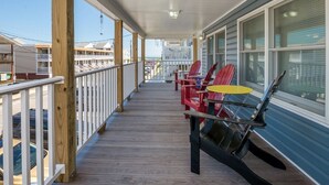 Um deck de madeira com guarda-corpo, um alpendre coberto e uma fileira de cadeiras Adirondack.