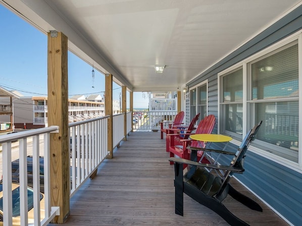 A wooden deck with a railing, a covered porch, and a row of Adirondack chairs. - BIG, beautiful; just steps to beach, OCEANblock! 2nd floor w/ocean & bay views. (Ocean City)