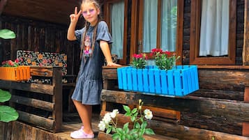 A rustic wooden cabin with a porch, a flower bed with white flowers, and a blue planter with red flowers.