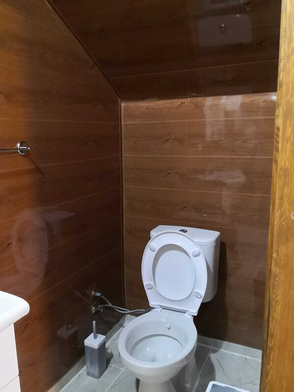 A small, modern bathroom with a wooden wall, a white toilet, and a marble floor. - Zeytindagi Bungalow (Edremit)