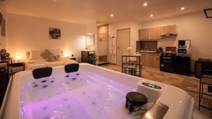 A modern hotel room with a large hot tub, a separate dining area, and a kitchenette.