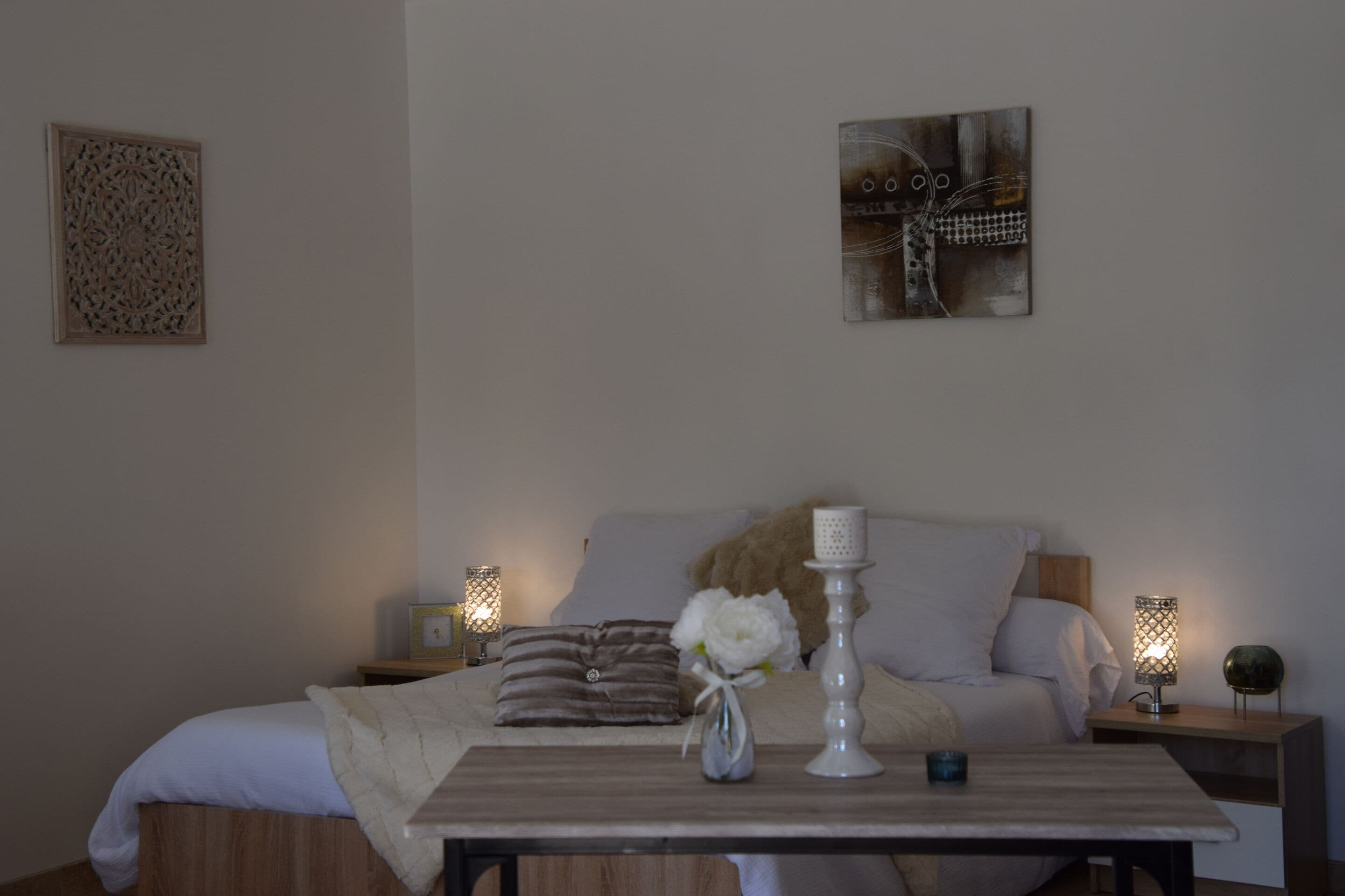 Ein ordentlich bezogenes Bett mit einem weiß-braun gestreiften Kissen, ein kleiner Blumenstrauß in einer Vase und zwei Nachttischlampen auf Holznachttischen.