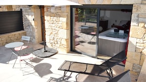 A stone-walled patio with a hot tub, a table, and chairs.