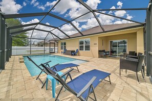 Zona de piscina techada al aire libre con sillas de descanso y una mesa de patio, rodeada por una estructura de metal.