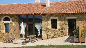 Un bâtiment en pierre avec un toit en tuiles, un banc en bois et une table à l’extérieur.