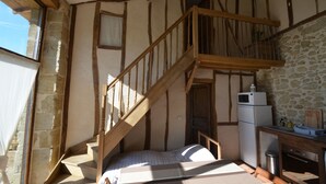 Une chambre avec un escalier en bois, un lit, un petit bureau et un mur en pierre.