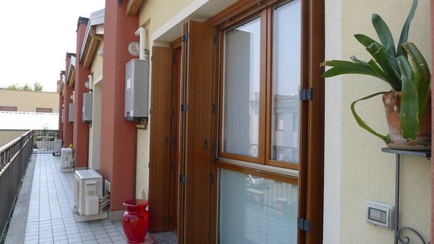 Ein Balkon mit roter Vase, Topfpflanze und einer Schiebetür.